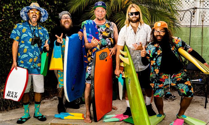 A six-member reggae band, posing in bright jams and Hawaiian shirts with boards and flippers