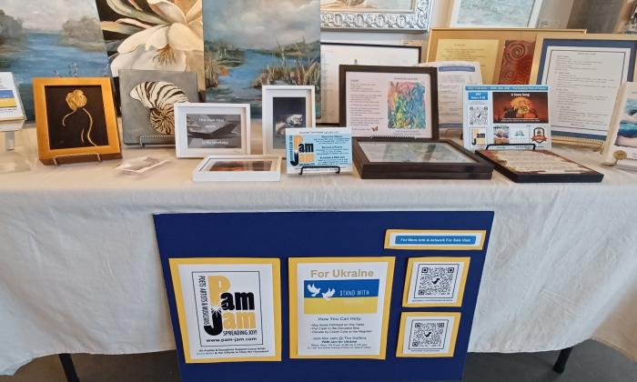 PAMJam for Ukraine event represented by a table with plaques and information on the fundraiser. 