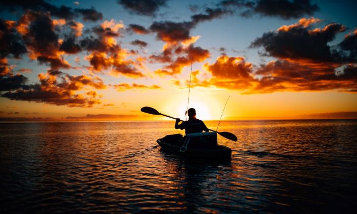 A man steers his kayak and navigates the water during sunset.