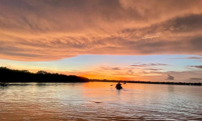 A man paddles in his kayak and enjoys the sunset. 