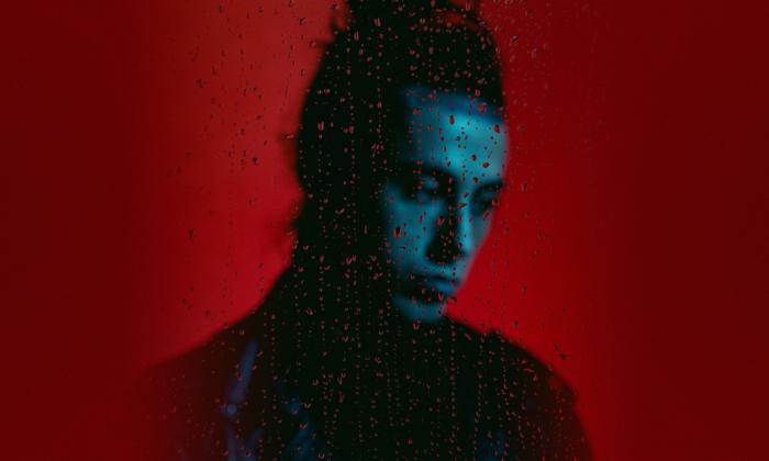 Lead singer Ronnie Radke poses with a solemn expression in front of a bright red background. 