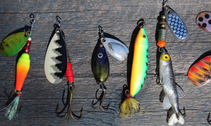 Colorful bait and fishing hooks are on a wooden board. 