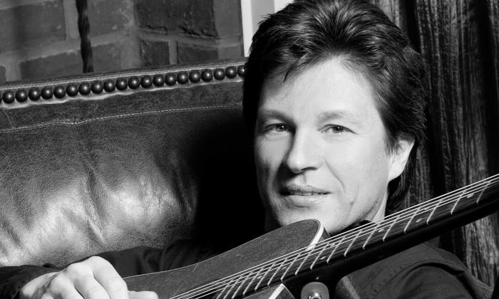 B&W Close up of a middle-aged white man sitting on a leather chair with a guitar propped across his body
