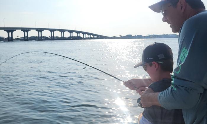 A man and a boy holding a rod that's bending under the weight of a fish