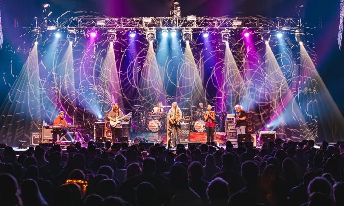 Band members of the Dark Orchestra performs live on a stage with colorful lights. 