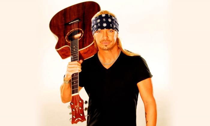 Bret Michaels holds his guitar upside down in front of a white background. 