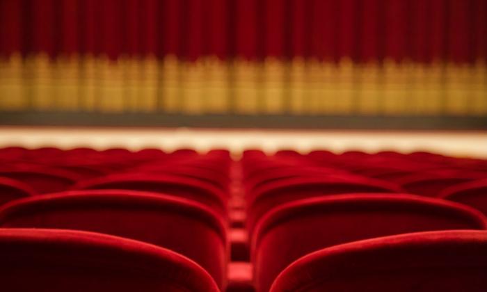 A row of red chairs are positioned in front of a theater curtain. 