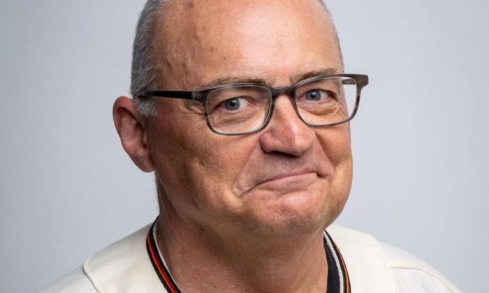 Brad Upton wears glasses and smiles in front of a white backdrop. 