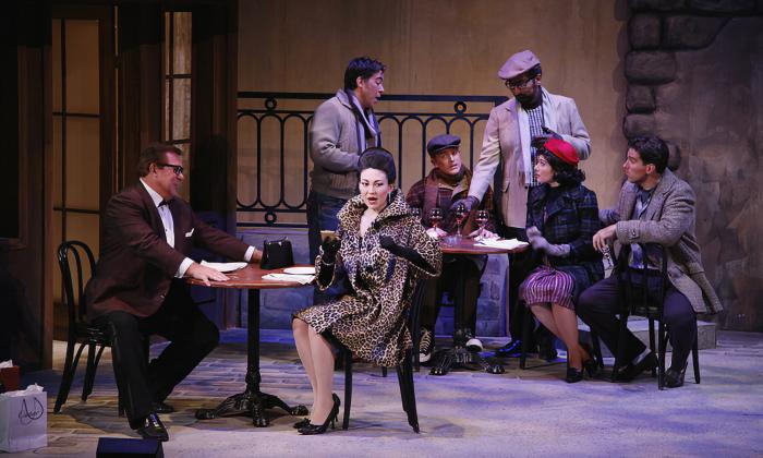 The cast of La Boheme, seated on stage in a French Bistro setting