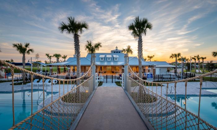 A bridge over a pool, leading to a clubhouse framed by palm trees at sunset at the Silverleaf community