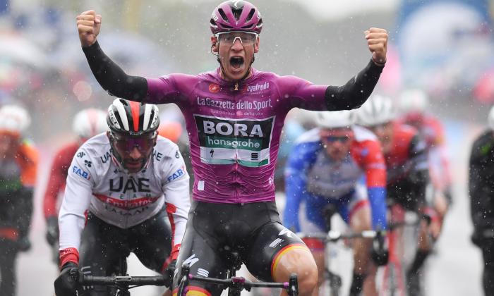 Cyclist in pink jersey celebrating victory with raised fists at Giro d'Italia race, with competitors in background