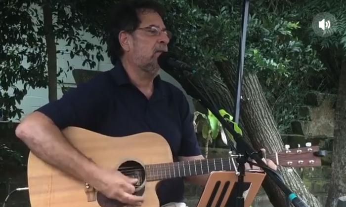 Musician Wayne Lake shown playing his guitar in a garden