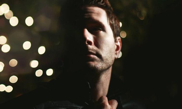A headshot of Owl City posing in front of a backdrop with bokeh. 