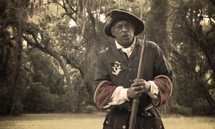 An older Black man dressed in the garb of a 1700s Spanish Soldier standing in the green space of Fort Mose Historic State Park.