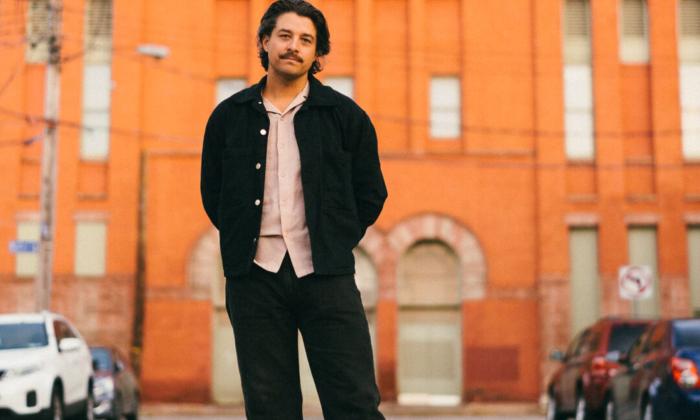 Matthew Logan Vasquez poses in front of an orange building. 