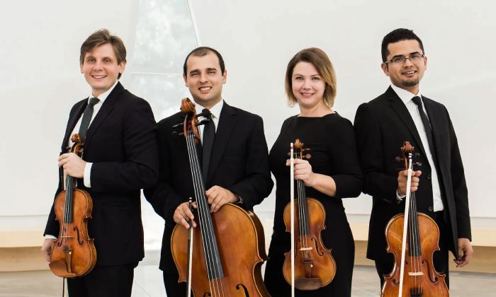 Members of the Con Brio String Quartet, stand holding their instruments on a white stage
