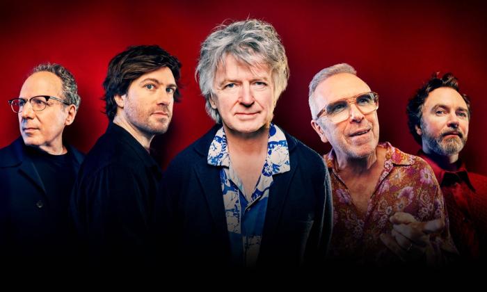 Bandmates from Crowded House pose in front of a red backdrop. 