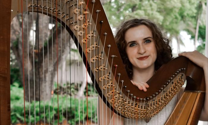 Isabelle Scott with her harp, in a garden of trees