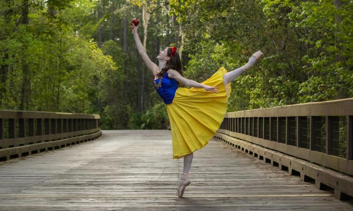 A ballet dancer dressed as Snow White, in blue and yellow, poses on a wooden boardwalk in St. Augustine