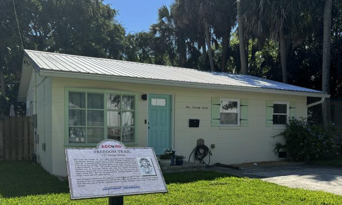 Yellow one-story cement block home with sea green details. In the foreground, the 177 Twine ACCORD Freedom Trail Marker.