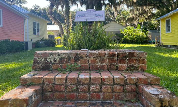 Looking upwards, grassy lawn with three delapidated brick steps leading to a historical marker.