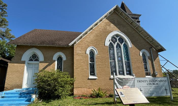Tan brick church with arched windows and a bright blue side staircase. ACCORD Freedom Trail marker in foreground. 