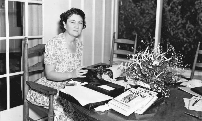 Author Marjorie Kinnan Rawlings at her table with a typewriter, showing a copy of the book "The Yearling"