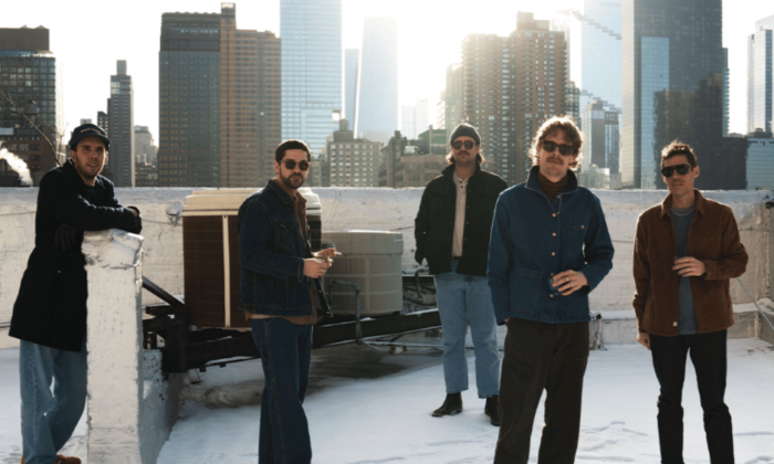 Bandmates from Caamp pose on a rooftop with buildings and skyscrapers as their backdrop.