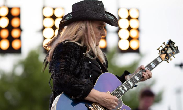 Melissa Etheridge wears a black cowboy hat and matching blouse while performing on stage for fans. 