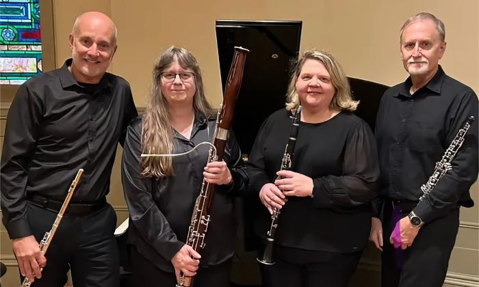Four members of a woodwind quartet, wearing black and holding their instruments are arrayed before a grand piano,