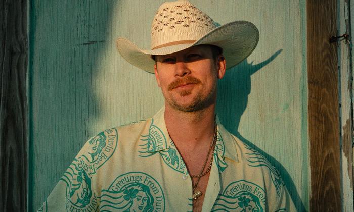 Brian Kelley poses in a white cowboy hat in front of a light blue backdrop.