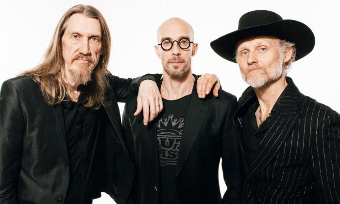 Bandmates from The Wood Brothers pose in black while standing in front of a white backdrop.