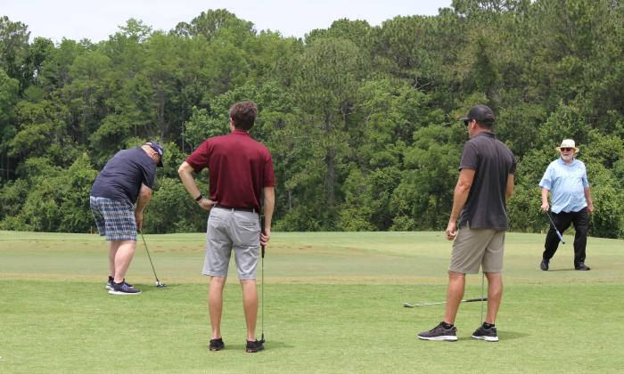 Four men at the green, with one putting, during a charity golf tournament
