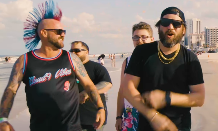 Members of Cloud 9 Vibes stroll down a beach as they perform a song together.