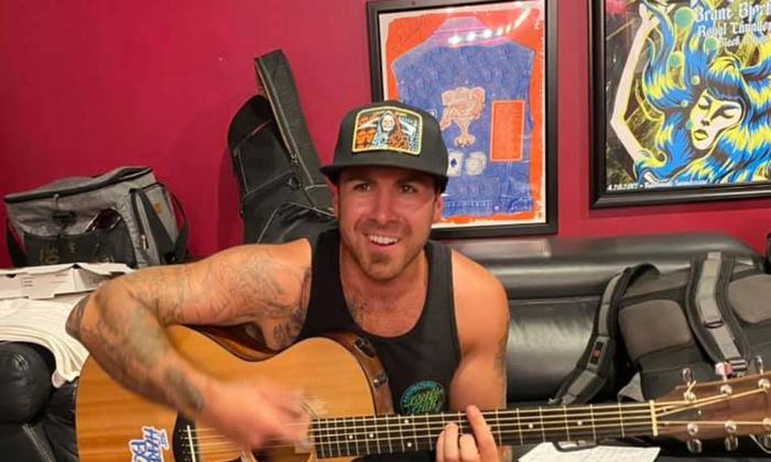 Musician Kyle Smith smiling, and playing a guitar, in a music studio