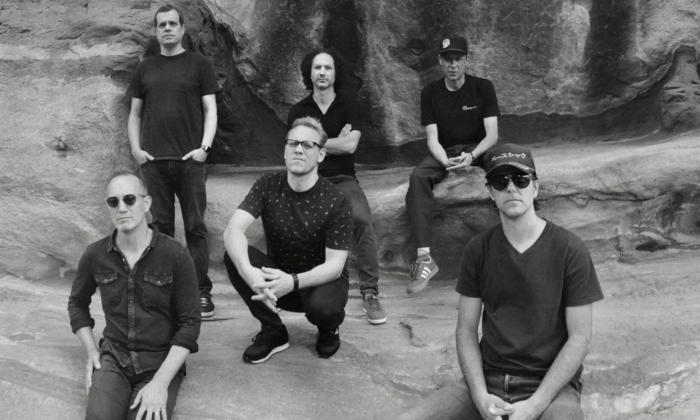Bandmates from Umphrey's McGee sit on rocks while posing in dark clothing and glasses.