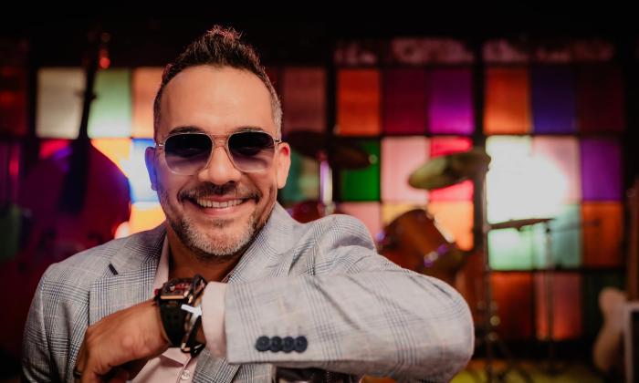 The singer and songwriter Helvis Rangel leaning on a countertop in a bar with a colorblock stained glass window