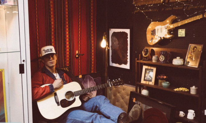 Hudson Westbrook sits in a chair and poses with his guitar.