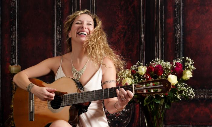 Zaza in a white dress, holding her guitar and singing.