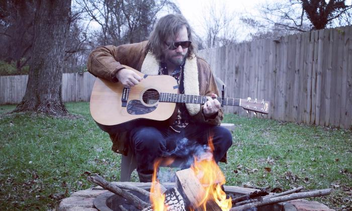 James McNair, singer and songwriter, playing his guitar in his backyard near a fire pit
