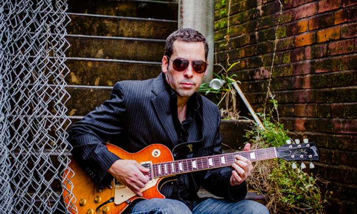 Albert Castiglia wears glasses while strumming his guitar.