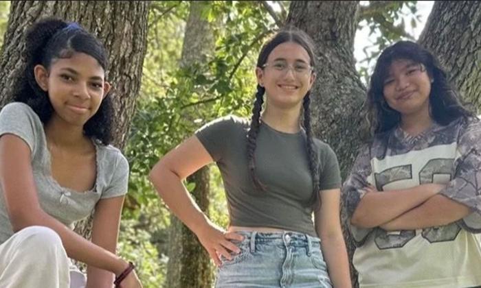 Trio girl band standing in front of trees. 