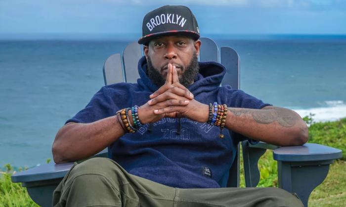 Talib Kweli sits back in a chair musing in front of an open ocean. 