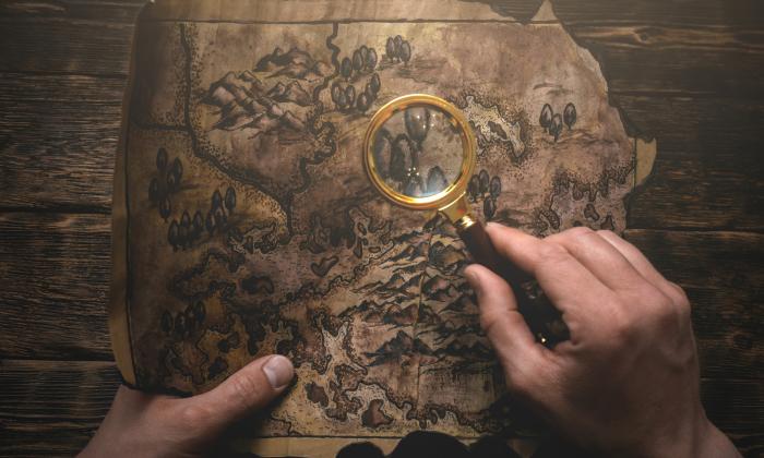 two hands holding an old map, one hand has a magnifying glass