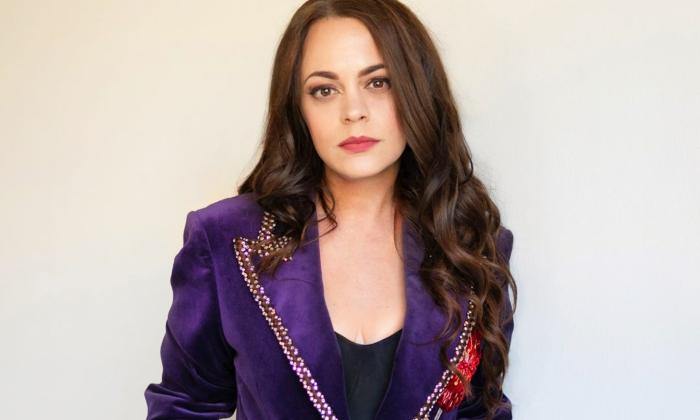Mindy Smith stands before a white backdrop, striking a pose in a royal purple blazer.