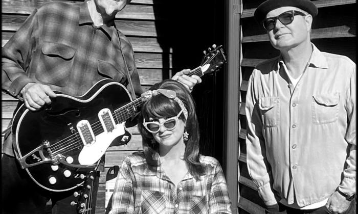 Bandmates from Southern Culture on the Skids smile and pose in front of a wooden house.