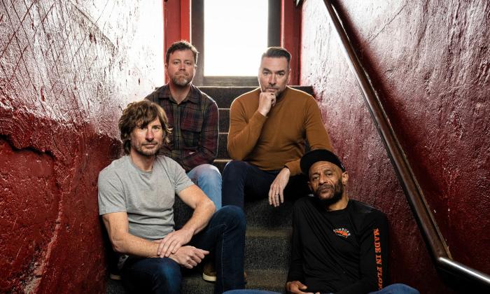 The four members of the New Mastersounds, sitting on stairs