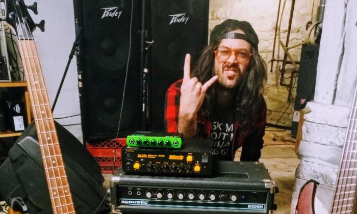 A musician at his mixer, with hat backwards, tongue out, and showing the sign of the horns
