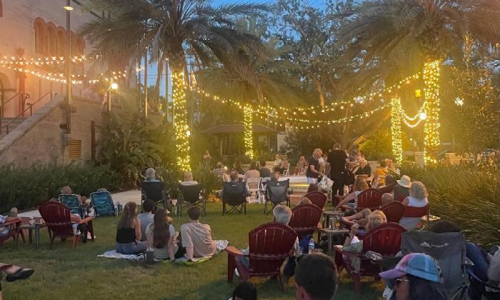 People gathered on a lawn in chairs and on the grass, listening to a jazz group.