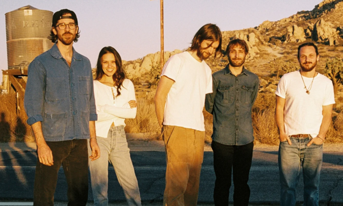 The members of Mt. Joy, dressed in white and blue shirts, pose together against a scenic natural backdrop.